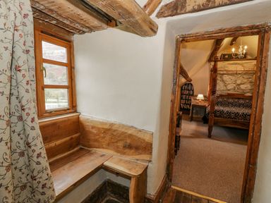 A corner with wooden bench seating and window with floral curtains leading into a bedroom with a four-poster bed and stone wall at Ysgubor in Dinas Mawddwy near Dolgellau