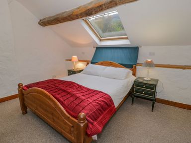 A bedroom with a wooden bed a red blanket two bedside tables with lamps and a skylight window at Ysgubor in Dinas Mawddwy near Dolgellau