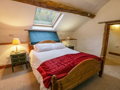 A bedroom with a wooden bed and red blanket under a skylight window at Ysgubor in Dinas Mawddwy near Dolgellau
