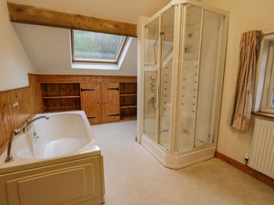A bathroom with a bathtub a glass shower enclosure wooden shelves and a skylight at Ysgubor in Dinas Mawddwy near Dolgellau