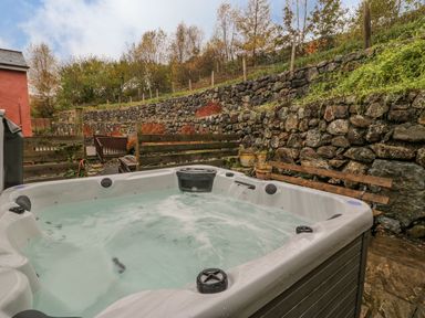 An outdoor hot tub with water jets next to a stone wall and wooden bench at Ysgubor in Dinas Mawddwy near Dolgellau