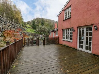 A wooden deck attached to a pink house with fenced edges and a stone wall on the left at Ysgubor in Dinas Mawddwy near Dolgellau
