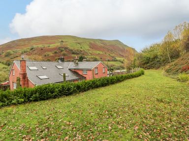 A red house with grey roof and skylights in a grassy area with hills and trees around at Ysgubor in Dinas Mawddwy near Dolgellau