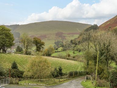 A rural landscape with green hills trees a gravel road and a gate at Ysgubor in Dinas Mawddwy near Dolgellau