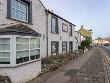 A street view of a row of white stone houses with small front gardens and a sidewalk in Keswick