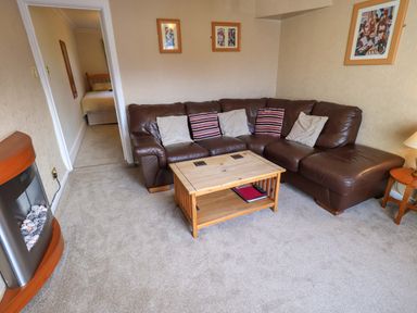 A living room with a brown leather corner sofa a wooden coffee table a fireplace and framed pictures on the wall at Lakeland View Lodge in Keswick