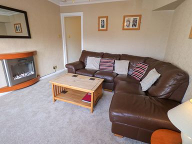 A living room with a brown leather corner sofa and a wooden coffee table at Lakeland View Lodge in Keswick