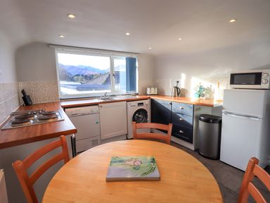 A kitchen with a round wooden table and chairs a window over the sink appliances including a dishwasher washing machine microwave and fridge at Lakeland View Lodge in Keswick