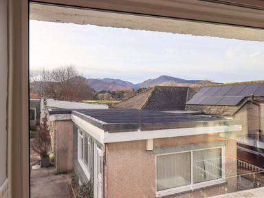 A view of rooftops with solar panels and distant hills seen through a window at Lakeland View Lodge in Keswick