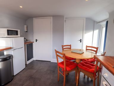 A kitchen with a round wooden table and four chairs with red cushions two white doors a microwave on a white refrigerator and a window at Lakeland View Lodge in Keswick