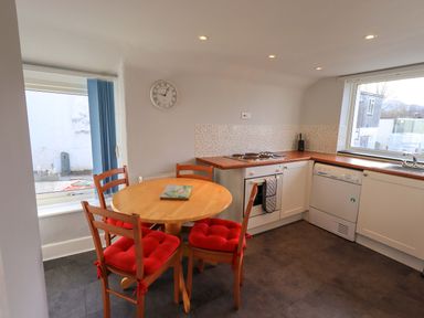 A kitchen with a round wooden table and four chairs with red cushions and appliances at Lakeland View Lodge in Keswick