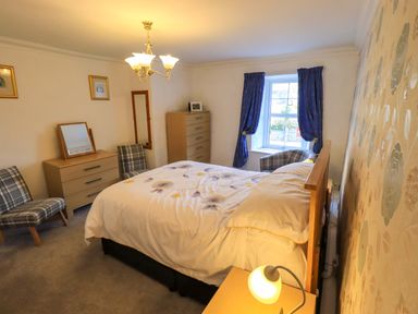 A bedroom with a double bed two dressers two plaid chairs a window with blue curtains and a nightstand lamp at Lakeland View Lodge in Keswick