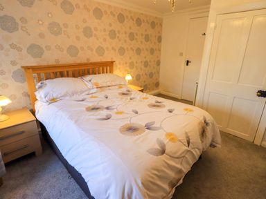 A bedroom with a double bed with floral bedding two bedside tables with lamps and a floral wallpaper at Lakeland View Lodge in Keswick