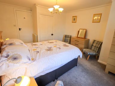 A bedroom with a bed a chest of drawers two chairs and a ceiling light at Lakeland View Lodge in Keswick