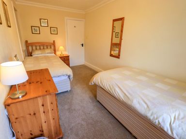 A bedroom with two single beds a wooden chest of drawers two lamps framed pictures and a mirror at Lakeland View Lodge in Keswick