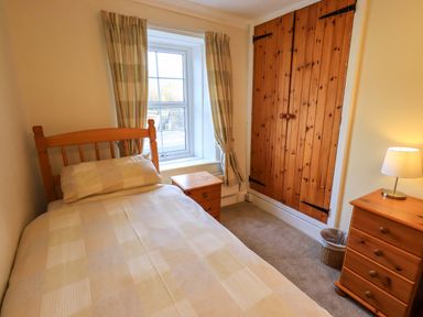 A small bedroom with single bed wooden nightstand wooden dresser lamp and built in wooden wardrobe at Lakeland View Lodge Keswick