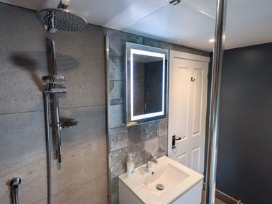 A bathroom with a shower head sink with a faucet illuminated mirror and a white door at Lakeland View Lodge Keswick