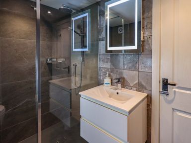 A bathroom with a glass shower enclosure an illuminated mirror above a white sink unit at Lakeland View Lodge in Keswick