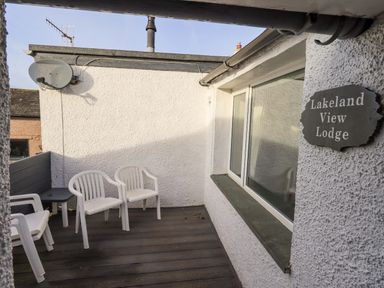 An outdoor balcony with white plastic chairs a small table and a sign reading Lakeland View Lodge at Keswick