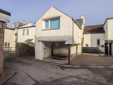 An exterior view of a white building with an open ground floor area and surrounding paved and gravel surfaces at Lakeland View Lodge in Keswick