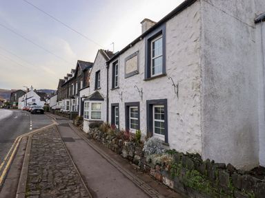 A row of stone and white painted houses along a street with parked cars and a stone sidewalk at Lakeland View Lodge in Keswick