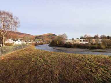 A river curving through a grassy area with houses on the left and buildings on the right at Lakeland View Lodge in Keswick
