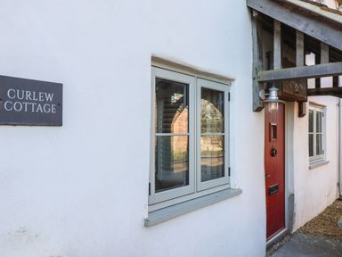 The exterior of a white cottage with a red door a window and a sign that says Curlew Cottage at Curlew Cottage in North Curry near Taunton