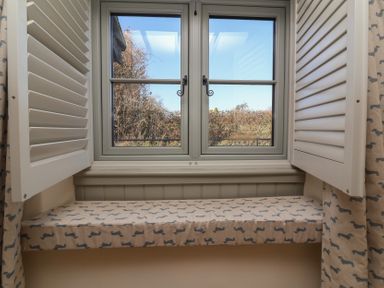 A window with open shutters and a cushioned window seat covered in fabric with a dachshund pattern at Curlew Cottage North Curry near Taunton