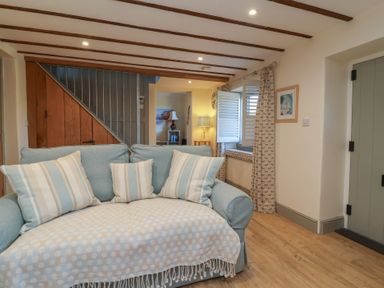 A sitting area with a light blue sofa with striped cushions near wooden staircase and shuttered window at Curlew Cottage in North Curry near Taunton