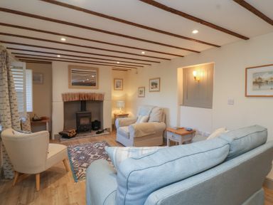 A living room with blue and beige chairs a wood burning stove and wooden beams on the ceiling at Curlew Cottage North Curry near Taunton