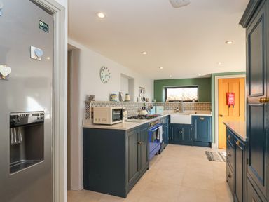 A kitchen with blue cabinets a stainless steel refrigerator a microwave a blue stove a white sink and a wooden door at Curlew Cottage in North Curry near Taunton