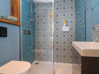 A bathroom with a walk-in shower featuring blue and patterned tiles a toilet a sink and a wall-mounted ceramic bowl at Curlew Cottage in North Curry near Taunton