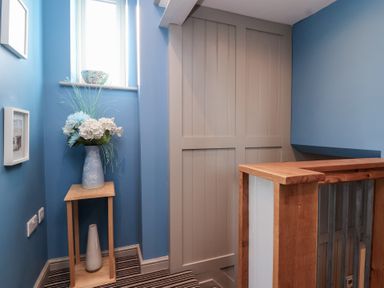 A small corner with blue walls a wooden stand holding vases and a staircase railing in Curlew Cottage North Curry near Taunton