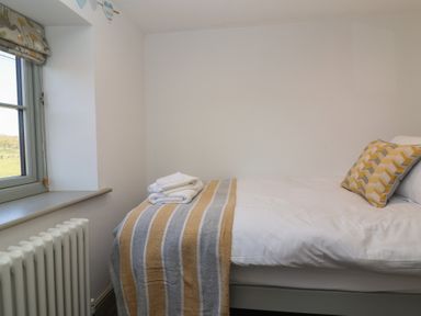 A bedroom with a bed with white linens a striped blanket and a patterned pillow by a window at Curlew Cottage in North Curry near Taunton