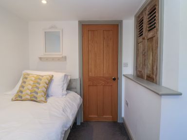 A bedroom with a bed a wooden door a wall mirror and wooden shutter at Curlew Cottage in North Curry near Taunton