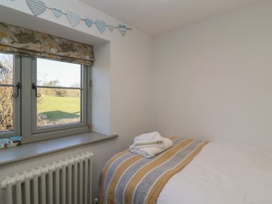 A bedroom with a window overlooking a field a bed with folded towels on a striped blanket at Curlew Cottage in North Curry near Taunton