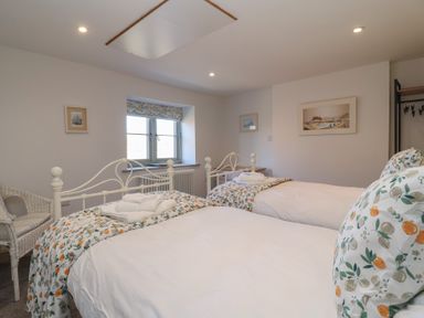 A bedroom with two single beds white bedding floral pillows a window and a wicker chair at Curlew Cottage in North Curry near Taunton