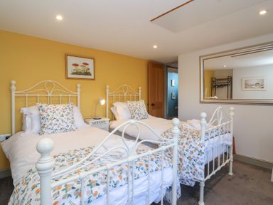 A bedroom with two single beds white metal frames floral bedding and a yellow accent wall at Curlew Cottage in North Curry near Taunton