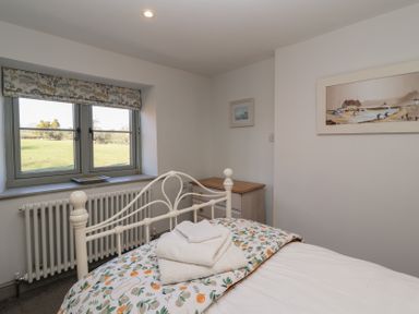 A bedroom with a metal bed frame white towels on the bed a window with a floral valance and a small dresser on the side at Curlew Cottage in North Curry near Taunton