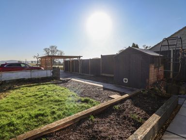 A garden with a grassy area a wooden shed a carport and a parked red car at Curlew Cottage in North Curry near Taunton