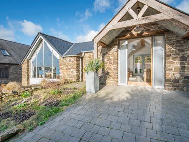 Stone exterior cottage with large windows and potted plant on paved patio at Leeward Cottage in Cosheston near Pembroke Dock