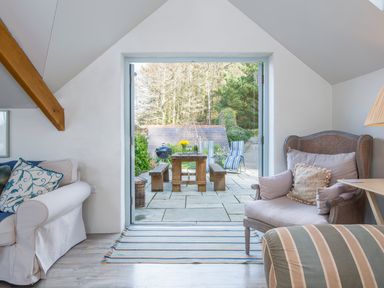 A sitting area with upholstered chairs and sofa leading to a patio with wooden picnic table at Leeward Cottage in Cosheston near Pembroke Dock