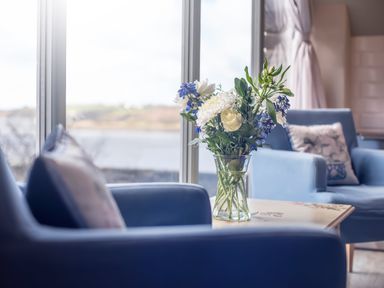 A living room with a bouquet of flowers on a table between blue armchairs at Leeward Cottage in Cosheston near Pembroke Dock