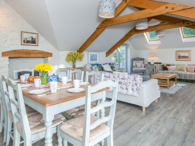 A dining table set with plates cups and flowers next to a living area with sofas chairs and wooden beams on the ceiling at Leeward Cottage in Cosheston near Pembroke Dock