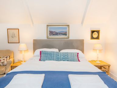A bedroom with a bed between two bedside tables each with a lamp and paintings above at Leeward Cottage in Cosheston near Pembroke Dock
