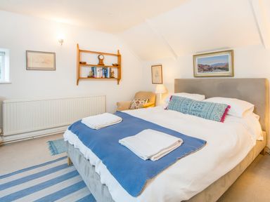 A bedroom with a double bed a blue blanket on the bed a chair and shelves with books at Leeward Cottage in Cosheston near Pembroke Dock
