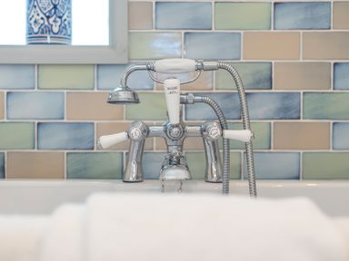 A bathtub faucet with shower attachment and colored tiled wall in a bathroom at Leeward Cottage in Cosheston near Pembroke Dock
