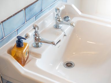 A white ceramic sink with two chrome taps and a yellow soap dispenser at Leeward Cottage in Cosheston near Pembroke Dock