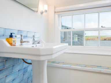 A bathroom sink with blue tiles near a window showing a waterfront view at Leeward Cottage in Cosheston near Pembroke Dock