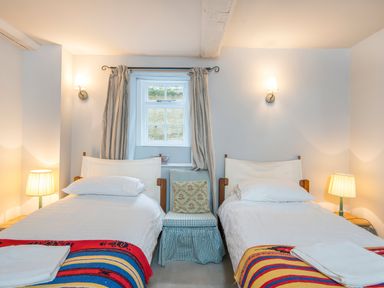 A bedroom with two single beds bedside tables lamps and a window at Leeward Cottage in Cosheston near Pembroke Dock